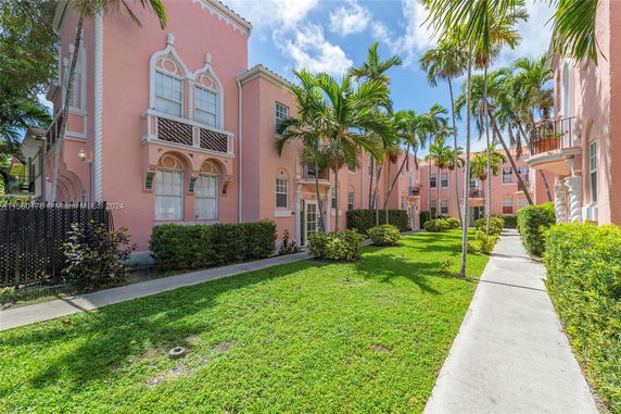 Front view of a pink multi-story residential building with ornate window designs and tropical landscaping.