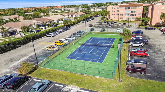 Outdoor tennis court with surrounding parking area and nearby residential buildings.