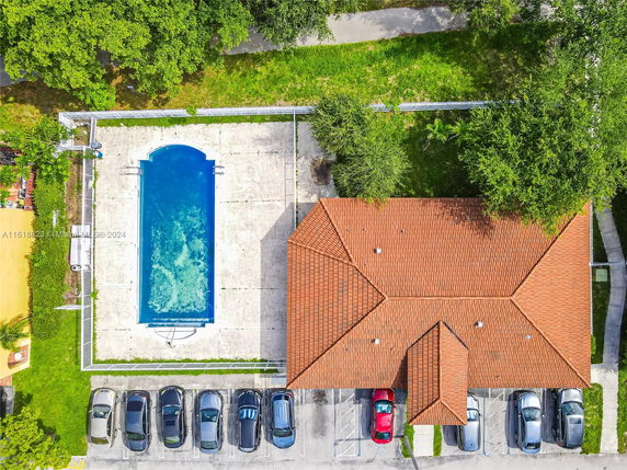 Aerial view of a rectangular swimming pool adjacent to a building with a red-tiled roof and a parking area.