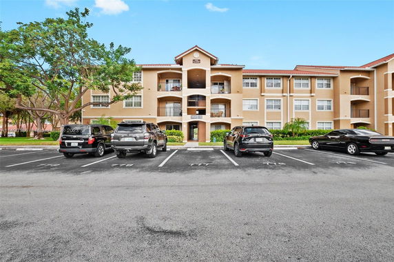 Front view of a three-story residential building with a parking lot in front.