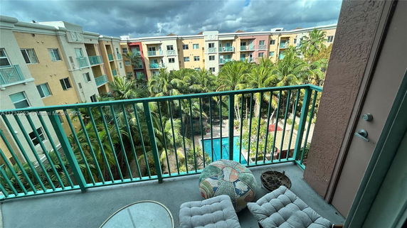 View from a balcony overlooking a garden and swimming pool surrounded by apartment buildings.