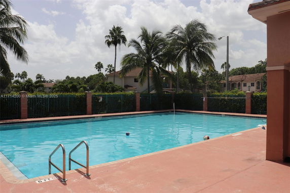 Outdoor swimming pool with surrounding fence and palm trees.