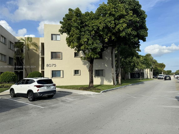 Front view of a multi-story building with parking spaces and trees.