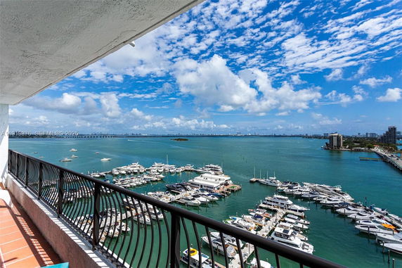 Panoramic view from a building balcony showing a marina with multiple boats and a city skyline in the distance.