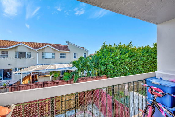 View from a balcony showing a residential building with a tiled roof and visible vegetation.