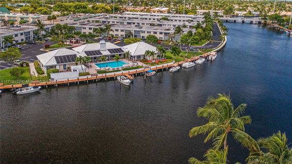Aerial view of a residential complex with a pool, solar panels on roofs, and boats docked along a waterway.
