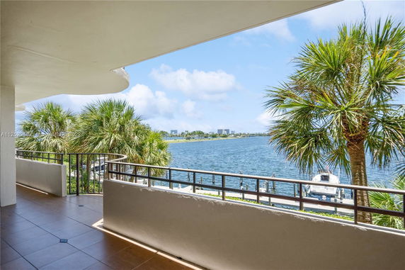 Balcony view overlooking water with palm trees and distant buildings.