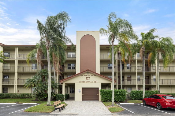 Front view of a multi-story residential building with balconies and palm trees.