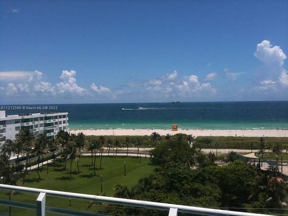 Panoramic view of a beach with an ocean, lawn, and buildings.