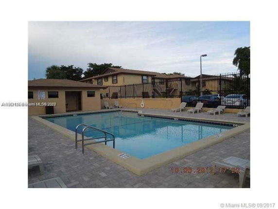 Outdoor swimming pool with surrounding buildings and lounge chairs.
