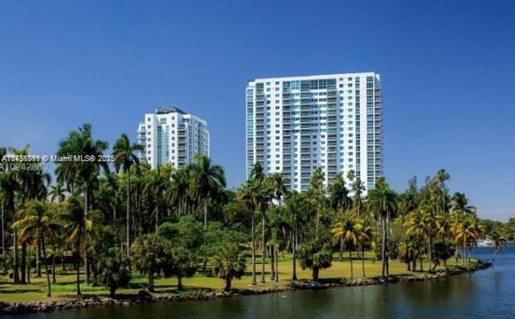 Tall apartment buildings surrounded by palm trees and a body of water.