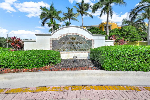 Front view of a luxury condominium entrance sign with palm trees in the background.