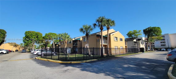 Front view of a multi-story apartment building with a fenced area and parking.