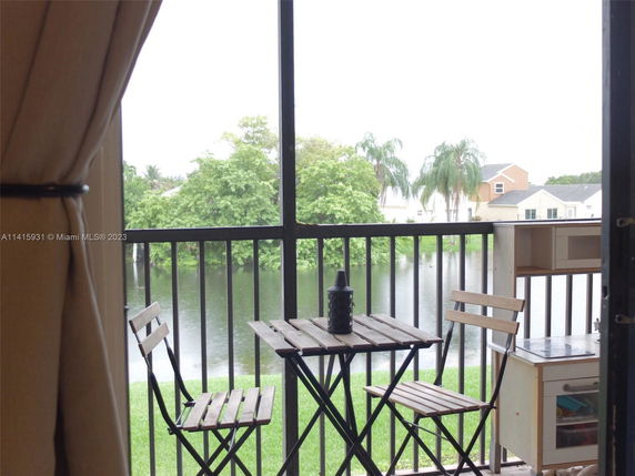 Balcony view with small table and chairs overlooking a water body and houses in the background.