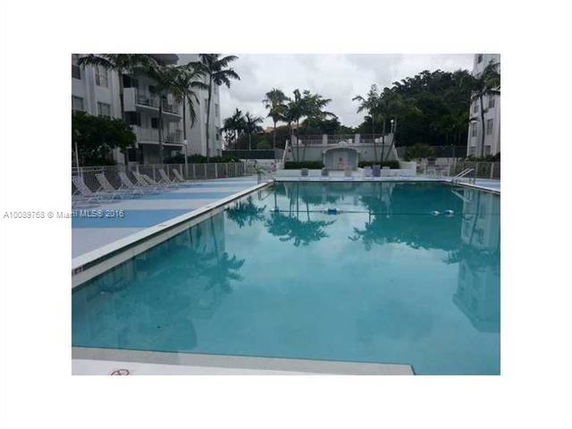 Outdoor swimming pool area surrounded by buildings and palm trees.