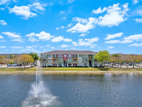 Front view of a multi-story building with colorful facade, adjacent to a water body with a fountain.