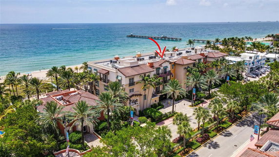 Aerial view of a beachfront building complex with palm trees and ocean in the background.