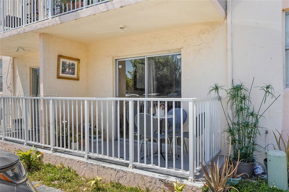 Front view of a lower-level apartment balcony with white railing and outdoor seating.