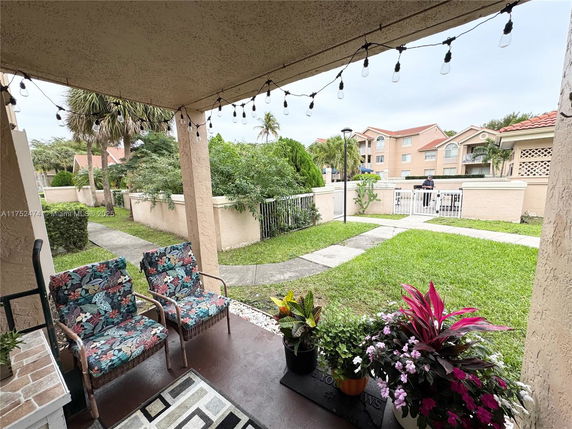 View from a covered porch with chairs overlooking a garden and neighboring buildings.