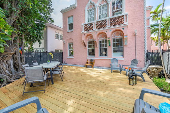 Outdoor view of a two-story pink house with arched windows and a wooden deck with patio furniture.