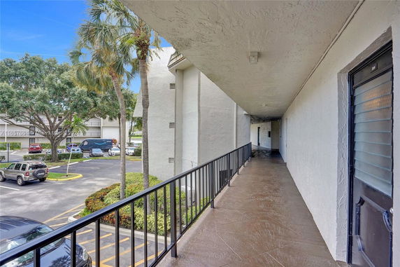 View from a balcony over a parking area with cars and palm trees.