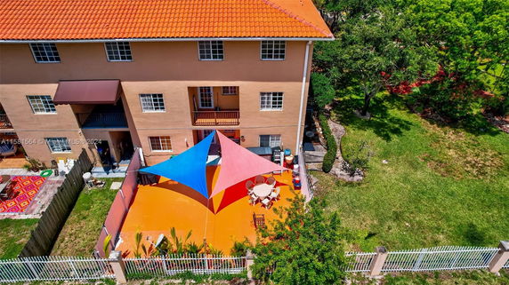 Aerial view of a building with a red-tiled roof and a fenced outdoor area with shade sails.
