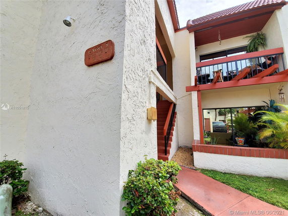 Front view of a two-story building with a red-tiled roof and an outdoor staircase.