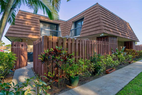 Front view of a two-story house with a wooden fence and brown roof panels.