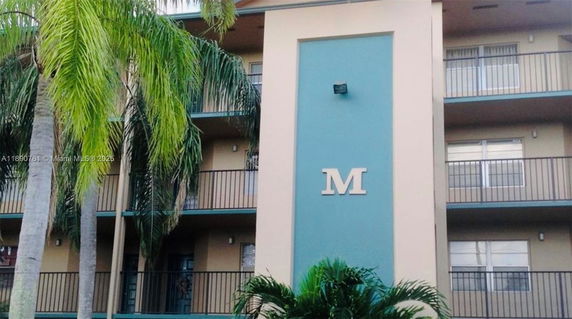 Front view of a multi-story building with balconies and palm trees.