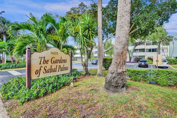 Front view of The Gardens of Sabal Palms building with surrounding palm trees and parking area.