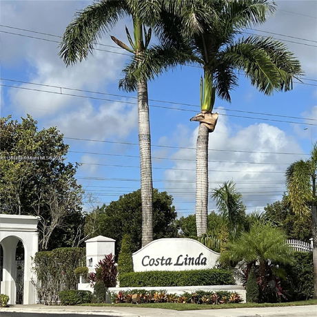Front view of a gated entrance marked 'Costa Linda' with palm trees.