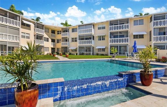 Outdoor view of a multi-story apartment building with balconies and a large swimming pool in front.