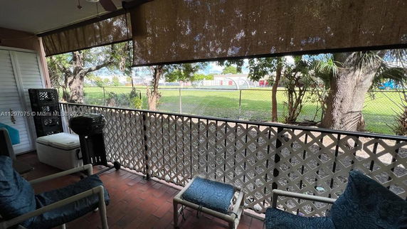 View from a covered patio with seating, overlooking a fenced grassy area with trees.