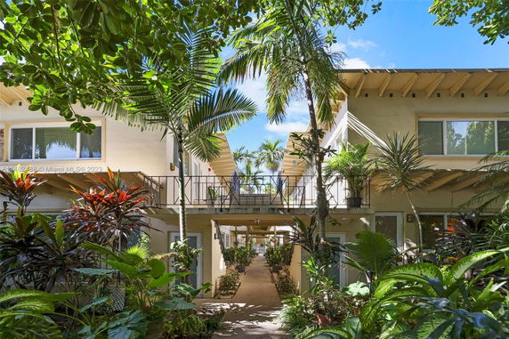Front view of a two-story building with balconies and lush vegetation.
