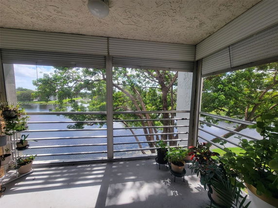 Balcony view with railing, potted plants, and trees in the background overlooking a water body.