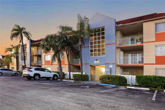 Front view of a multi-story apartment building with balconies and a parking area.