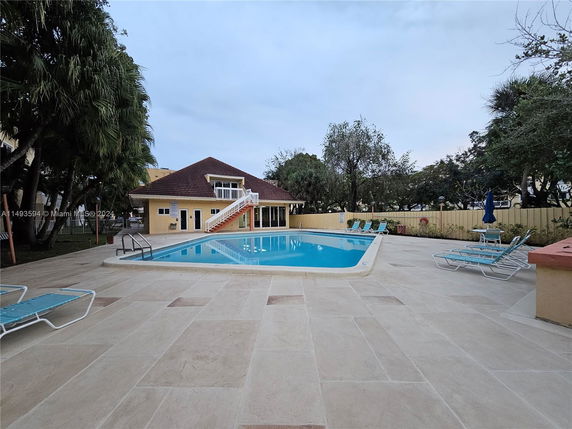 Outdoor swimming pool area with lounge chairs and a building in the background.