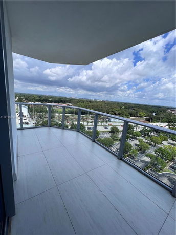 Balcony view from a high-rise building overlooking a cityscape and greenery.