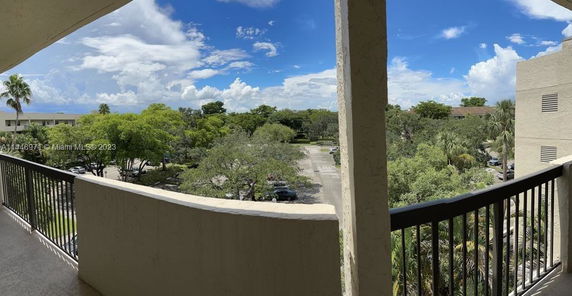 Panoramic view from a balcony overlooking a parking area and trees.