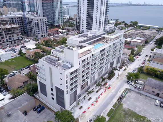 Aerial view of a multi-story residential building with a rooftop pool and surrounding urban development.