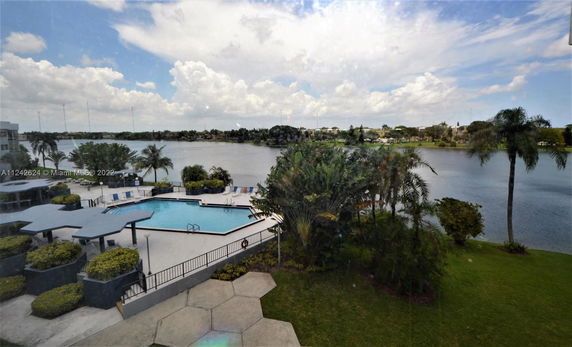 View of an outdoor swimming pool beside a lake, surrounded by landscaped greenery.