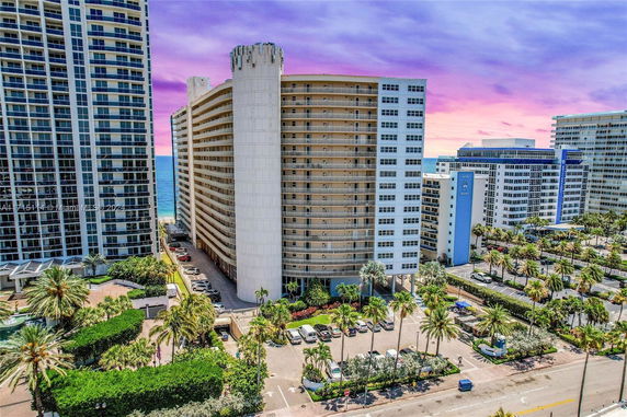 Front view of a high-rise building with a cylindrical tower and ocean in the background.