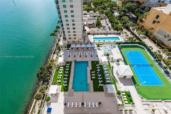 Rooftop view featuring a swimming pool, tennis courts, and lounge areas adjacent to a high-rise building.