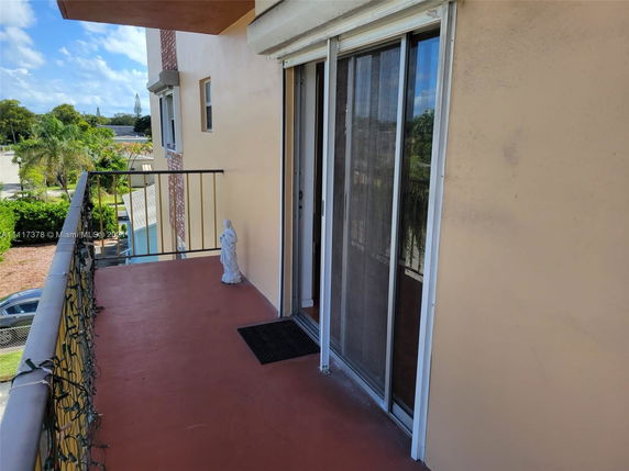 Balcony area with a sliding glass door, overlooking a garden and trees in the background.