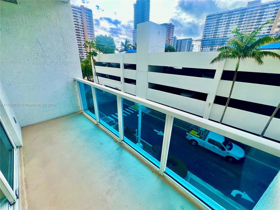 Balcony view overlooking a street with nearby tall buildings and palm trees in the background.