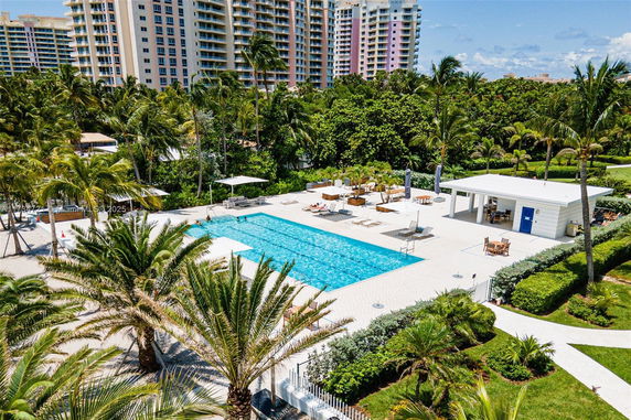 Outdoor swimming pool surrounded by palm trees with high-rise buildings in the background.