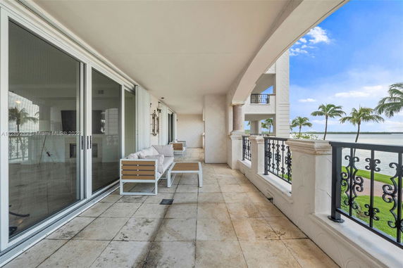 View from a building showing a spacious balcony with outdoor seating and a waterfront landscape.