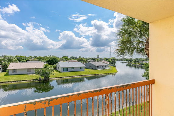 View from a balcony overlooking a waterway and houses with a palm tree partially visible.
