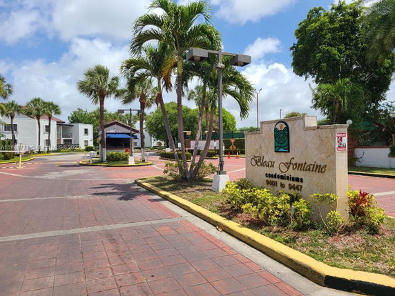 Entrance view of a condominium complex named Bleau Fontaine with palm trees and paved driveway.