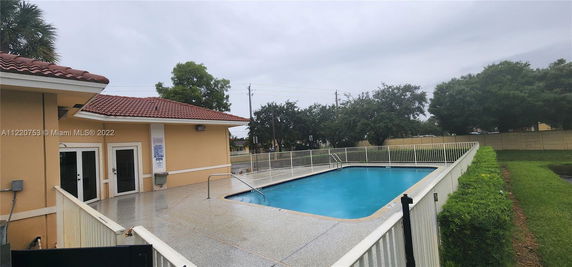 Outdoor swimming pool with fenced area beside a building with a red-tiled roof.